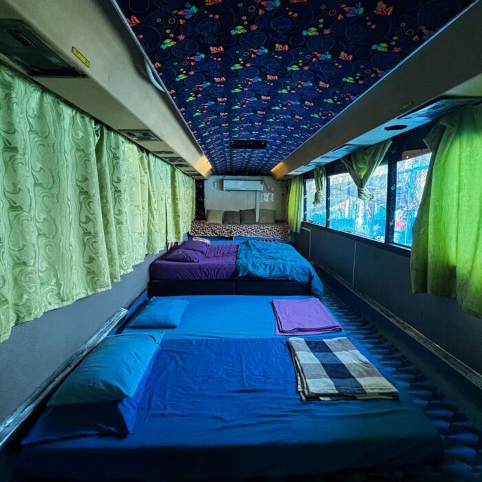 Ruang tidur di dalam Bas Lavender dengan deretan katil dan langsir hijau untuk privasi di Kuala Selangor Cabin Camp (KSCC).