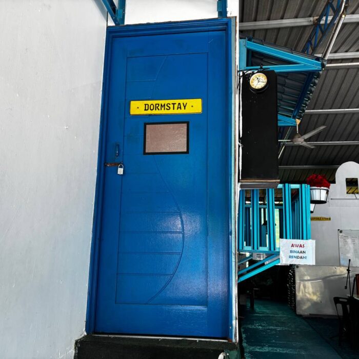 Pintu masuk berwarna biru untuk unit Dormstay dengan papan tanda 'DORMSTAY' yang jelas di Kuala Selangor Cabin Camp (KSCC).
