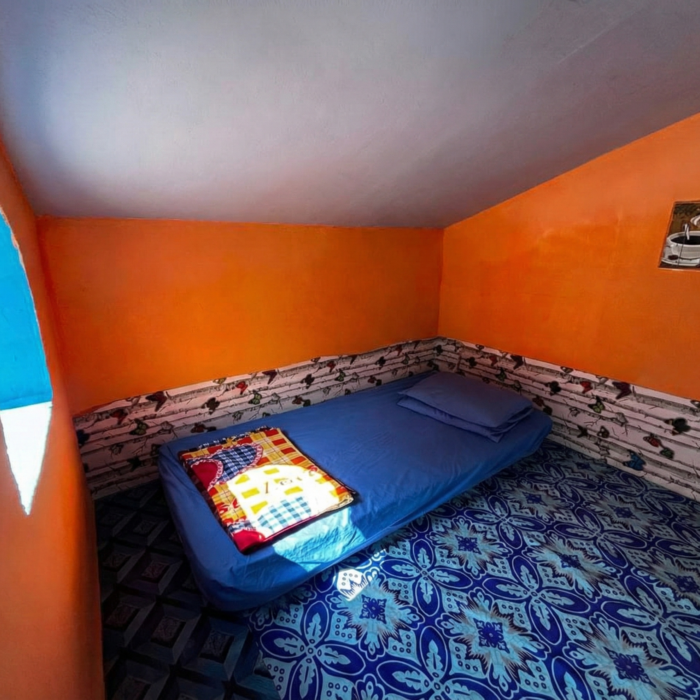 Ruang dalaman Hobbitstay dengan dinding oren yang ceria, lantai corak biru, dan kipas angin di Kuala Selangor Cabin Camp (KSCC).