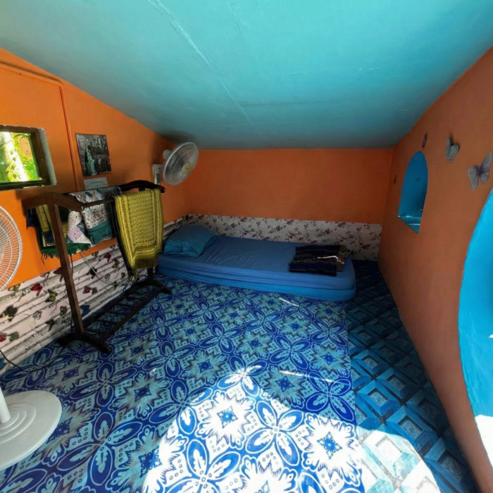 Ruang dalaman Hobbitstay dengan dinding oren, lantai corak biru, dan kipas angin di Kuala Selangor Cabin Camp (KSCC).