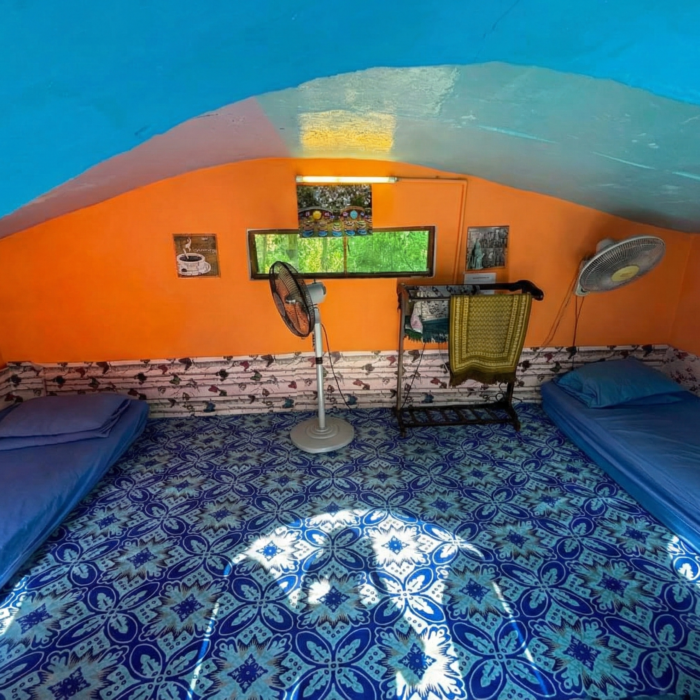 Ruang dalaman Hobbitstay dengan dinding berwarna oren dan biru, dilengkapi katil serta kipas angin.